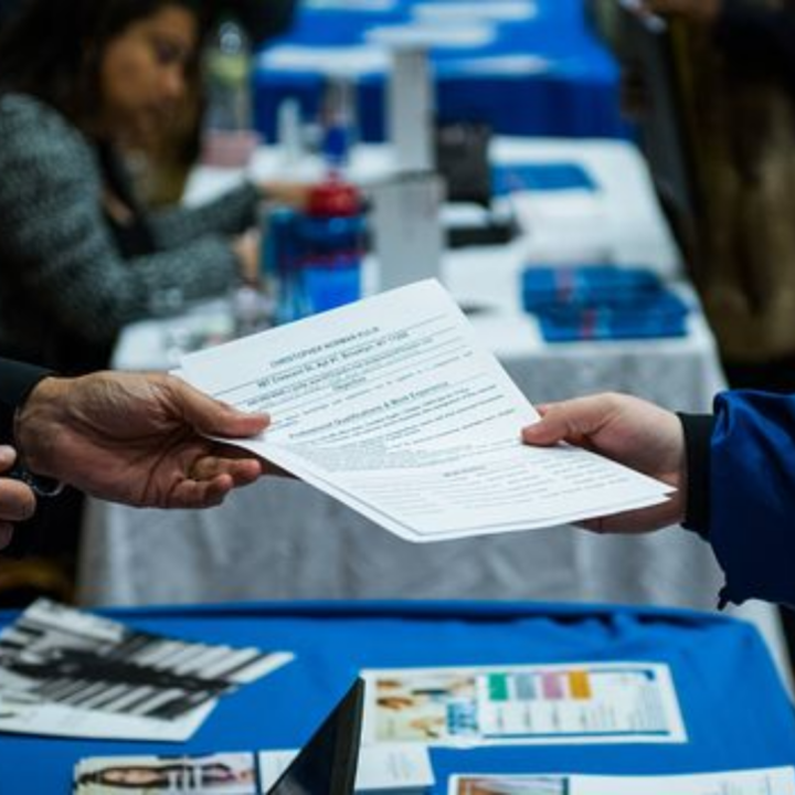 Job seeker handing a resume to a recruiter across a table at a career fair