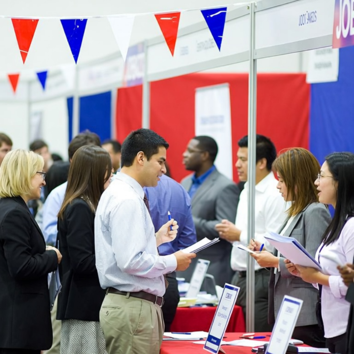 Job seekers networking with recruiters at a career fair with red, white, and blue booth displays
