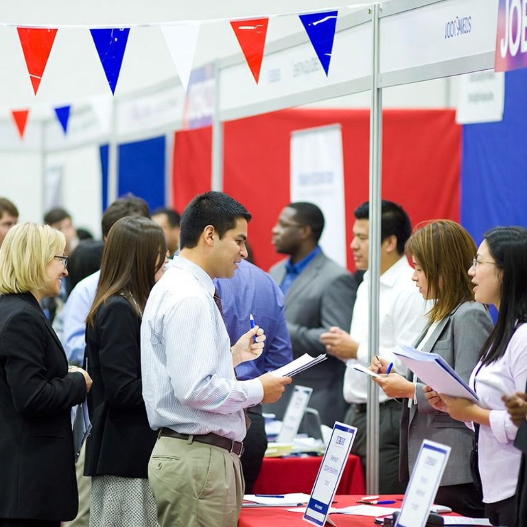 Job seekers networking with recruiters at a career fair with red, white, and blue booth displays