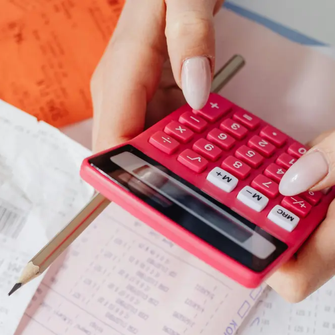 Close-up of hands using a pink calculator over financial documents and a pencil