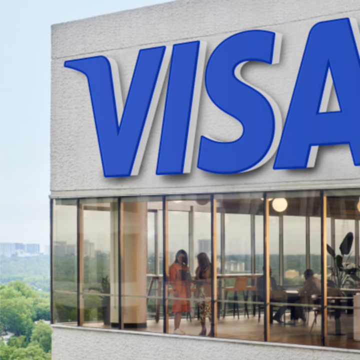 Visa corporate office building exterior with large blue logo signage and glass-walled interior visible with employees