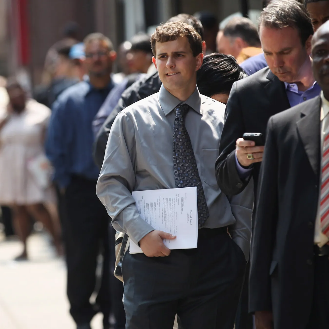 Job seekers in business attire waiting in line outdoors, with a young man holding a resume in the foreground