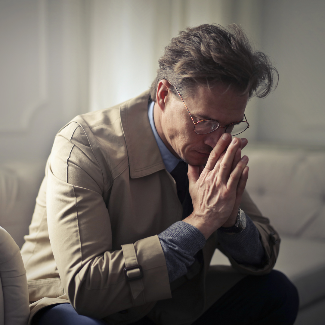 Male employee sitting with his head down and hands clasped together in a stressed or worried posture