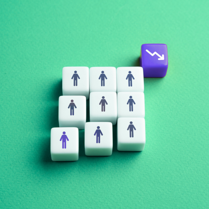 White cubes with person icons arranged in a declining staircase pattern next to a purple cube showing a downward arrow, representing workforce reduction or declining employment