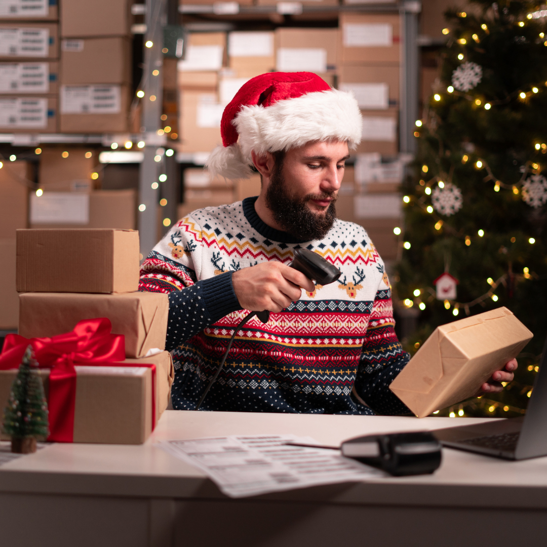 Warehouse worker in a Santa hat and holiday sweater scanning packages during the Christmas season rush