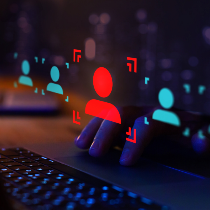Hand on a laptop trackpad selecting a highlighted red user profile icon among multiple digital candidate icons, representing hiring fraud or candidate fraud
