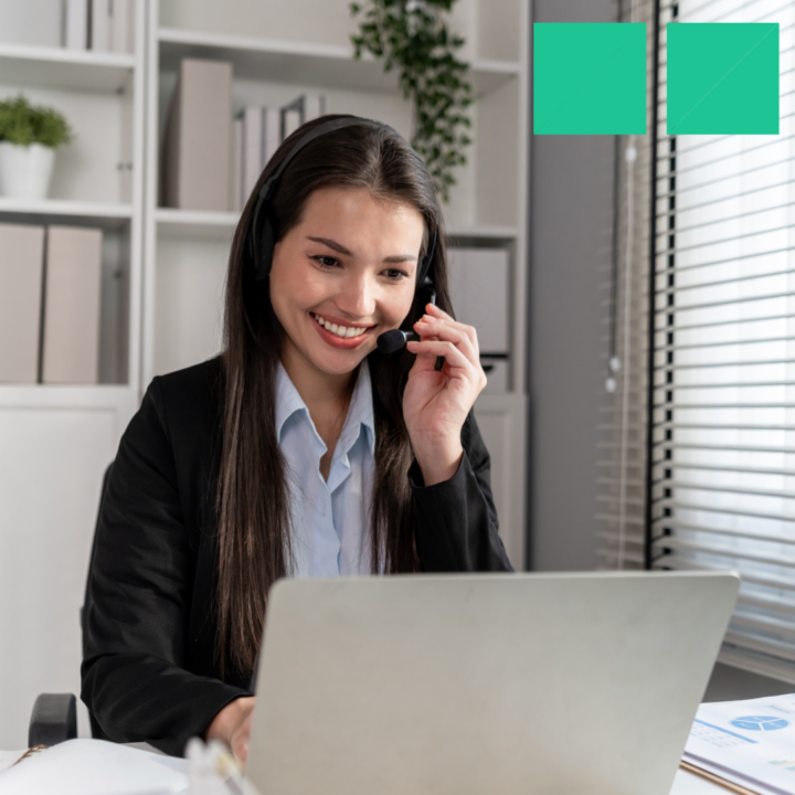 Smiling female recruiter wearing a headset and talking on a call while working on a laptop in an office