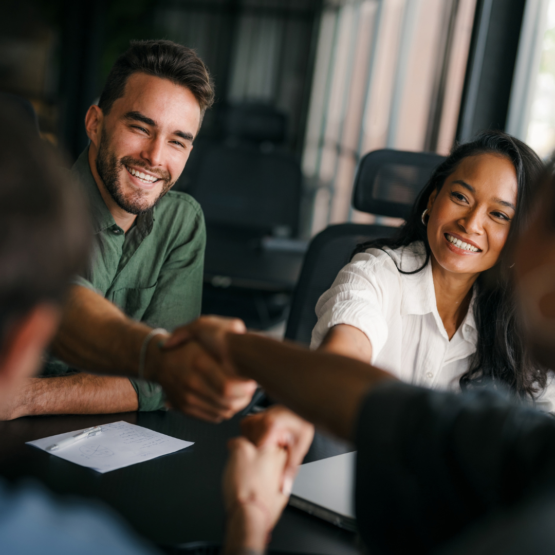 Two smiling professionals shaking hands across a conference table during a business meeting