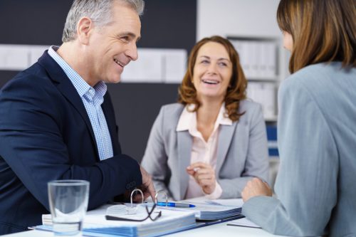 Baby boomers smiling and discussing business strategies around a desk in the office Baby boomers smiling and discussing business strategies around a desk in the office